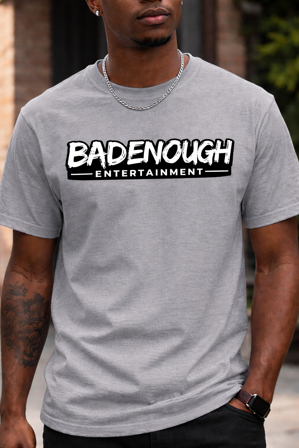 Person wearing a gray t-shirt with 'BADENOUGH ENTERTAINMENT' logo